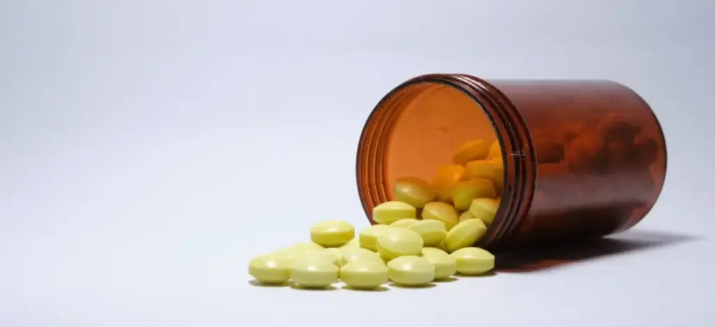 Prescription bottle tipped over with yellow stimulant pills spilled out, representing Adderall misuse and addiction risks.