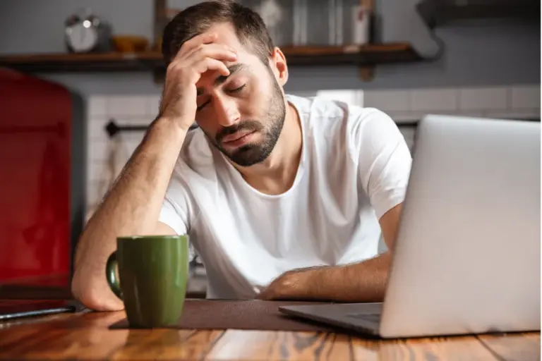 Exhausted professional sitting at a laptop with a headache, illustrating burnout and alcohol misuse among high-achieving professionals